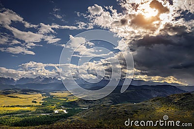 Majestic panorama of mountain plain on the background of snow-covered ridge before thunderstorm. Sun`s rays break through huge Stock Photo