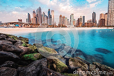 Rocks breakwaters in the foreground with the azure waters of the Persian Gulf and colorful skyscrapers in the Marina and Stock Photo