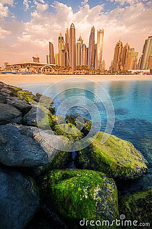 rocks breakwaters in the foreground with the azure waters of the Persian Gulf and colorful skyscrapers in the Marina and Stock Photo