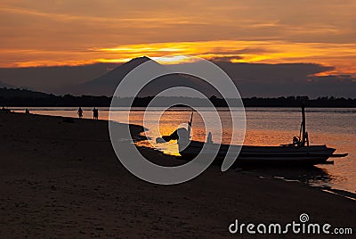 Majestic sunset on sea - golden sky, last sunbeams, dark volcano, black silhouette of fishing boat and walking people on beach. Stock Photo