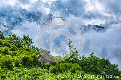 Majestic view of high mountains hidden by clouds and fog from a green cliff Stock Photo