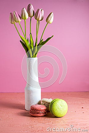 Makaroons on a pink background next to a bouquet of tulips in a white vase and copy space Stock Photo