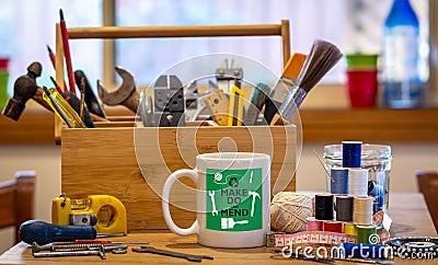Make do and mend logo on coffee mug surrounded by tools on cafe table top at repair cafÃ©, consumer activism, homespun movement Stock Photo