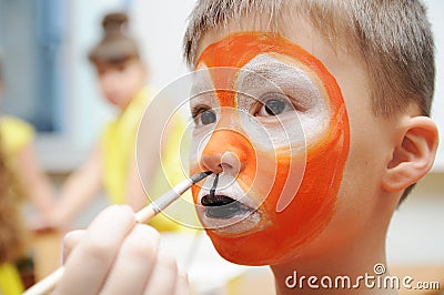 Make up artist making tiger mask for child.Children face painting. Boy painted as tiger or ferocious lion. Preparing Stock Photo