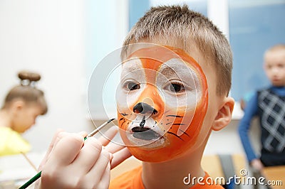 Make up artist making tiger mask for child.Children face painting. Boy painted as tiger or ferocious lion Stock Photo