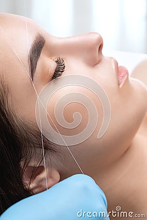 The make-up artist plucks eyebrows with a thread close-up. Women`s cosmetology in the beauty salon Stock Photo