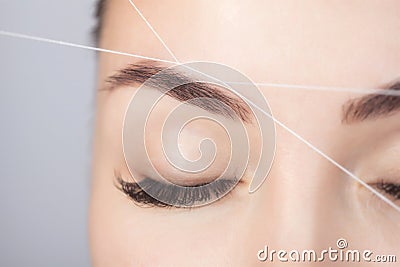 The make-up artist plucks eyebrows with a thread close-up. Women`s cosmetology in the beauty salon Stock Photo