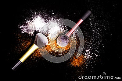 Make-up brushes with colorful powder on black background. Explosion stars dust with bright colors. White and orange powder. Stock Photo