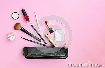 Make up products spilling out of a black varnished cosmetics bag on a pastel pink background Stock Photo