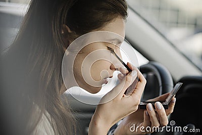 Make-up in transport. Breaking the law by a nice young woman. The brunette sits in the driver`s seat and applies shadows Stock Photo