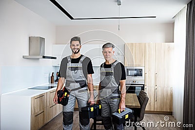 We make your life easier. Portrait of young and aged repairmen in uniform looking at camera with a smile, holding Stock Photo