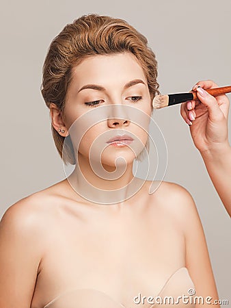 Makeup artist applies foundation on the skin of a girl with short blonde hair. Shot in a studio on a light background Stock Photo