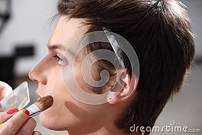 Makeup artist applying foundation with a brush, man in the dress Stock Photo