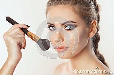 The Makeup artist paints powder on the girl`s face, completes make-up in the beauty salon. Stock Photo