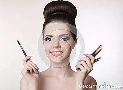 Makeup artist. Pretty teen girl with cute bun hairstyle and fashion beauty makeup, brunette holding brushes in hand isolated on w Stock Photo