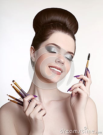 Makeup artist. Pretty teen girl with cute bun hairstyle and fashion beauty makeup, brunette holding brushes in hand isolated on w Stock Photo