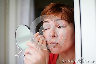 Makeup beauty care woman. Adult woman looks into mirror and putting eye pencil color on eyes Stock Photo