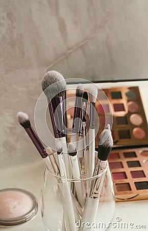 Makeup brushes stand in a glass against a background of makeup shadows Stock Photo