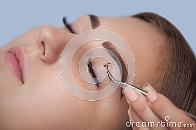 Makeup Master corrects, and strengthens eyelashes beams, holding out a pair of tweezers in a beauty salon. Stock Photo