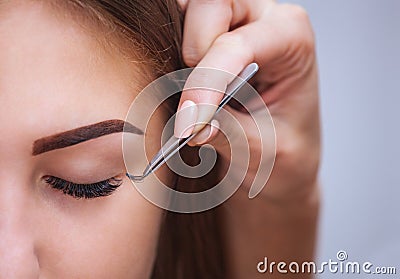 Makeup Master corrects, and strengthens eyelashes beams, holding out a pair of tweezers in a beauty salon Stock Photo