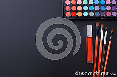 Makeup tools and accessories isolated on black background. Top view and mock up. Lipstick, eye shadows, make up brushes. Stock Photo