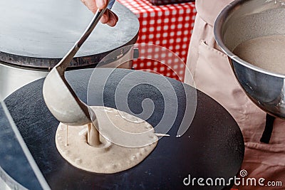 Making crepes pancakes in food market. A hand is making crepes outdoors pouring the batter onto a metal griddle Stock Photo