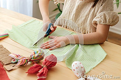 Making Easter eggs in the shape of a hare from textile. The girl prepares the fabric, cuts it with scissors. Home Stock Photo