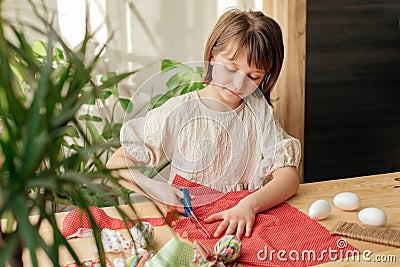 Making Easter eggs in the shape of a hare from textile. The girl prepares the fabric, cuts it with scissors. Home Stock Photo