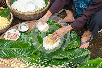 Making wrapping Chung Cake, the Vietnamese lunar new year Tet food outdoor with old woman hands and ingredients. Closed-up. Stock Photo