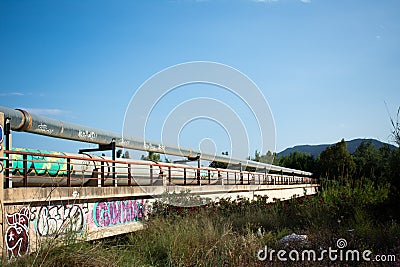 Old gas pipes for airport. Deteriorated gas pipes with graffiti running over a bridge. Copper pipes. Editorial Stock Photo