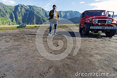 Malang, Indonesia - 25 March 2018 : Photo of an adult asian man pose next to a red jeep truck at Mount Bromo Editorial Stock Photo