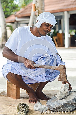 Maldivian construction worker in traditional national maldivian clothes cracking coral rocks with the axe Editorial Stock Photo