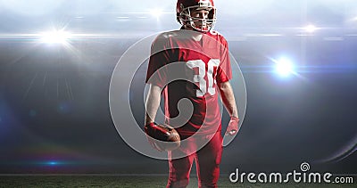 Male american football player holding ball standing at illuminated sports field Stock Photo