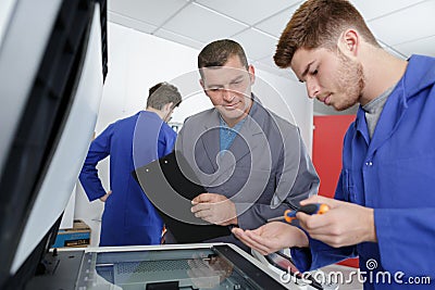 Male apprentice fixing printer supervisor watching Stock Photo
