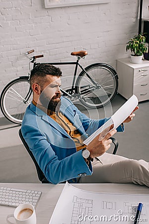 Male architect in blue jacket sitting and looking at paper Stock Photo