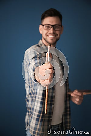 Male artist holding paintbrush on color background Stock Photo