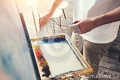 Male artist mixes colors on the palette in studio. Painter in workshop Stock Photo