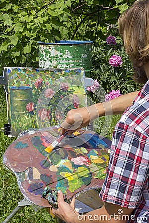 Male artist paint on plein air flowers pink peonies painting on nature Stock Photo