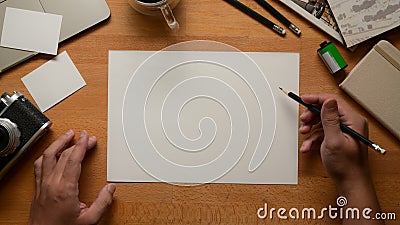Male artist working with blank sketch paper, pencils, camera and supplies on worktable Stock Photo