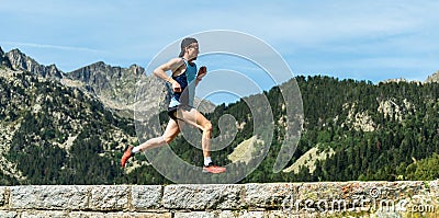 Male athlete running across a stone wall in the mountains Stock Photo