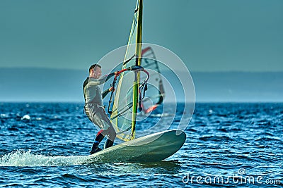 A male athlete is interested in windsurfing. He moves on a Sailboard on a large lake Stock Photo