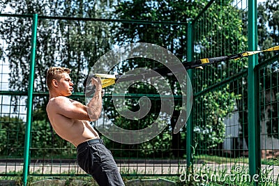 Male athlete, trains in fresh air, summer trx training, Balance motivation, tanned skin in shorts. Stock Photo