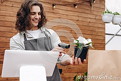 Male attractive florist selling flowerpot. Man assistant or owner in floral design studio, making decorations. Flowers delivery, Stock Photo