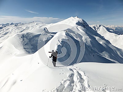 Male back country skier carrying his skis along a narrow snow ridge Stock Photo