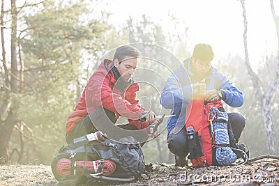 Male backpacker with friend whittling wood in forest Stock Photo