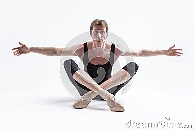 Male Ballerino Dancer Sitting While Practising Legs and Arms Stretching Exercices In Black Sportive Tights in Studio Stock Photo