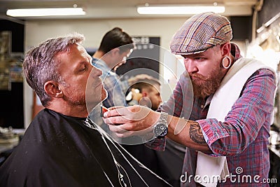 Male Barber Giving Client Shave In Shop Stock Photo