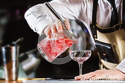 Male bartender is making cocktail pouring alchohol from jug to g Stock Photo