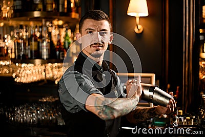 Male bartender with tattoo on the hand holding in hands a steel shaker with a deliciouds cocktail Stock Photo