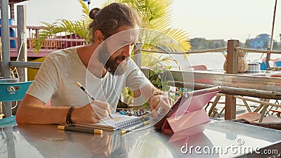 Male designer draw sketches in open air riverside cafe. Stock Photo